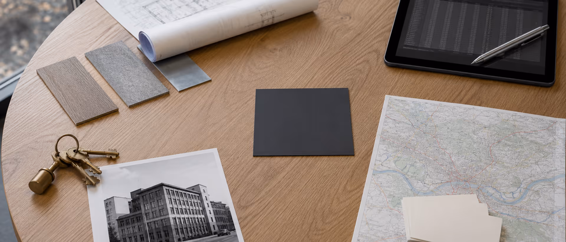 Konferenztisch mit vier Persona-Objektgruppen rund um eine zentrale Folienprobe — Architekturplan, Tablet, Schlüsselbund mit Bestandsfoto, Rhein-Main-Stadtplan